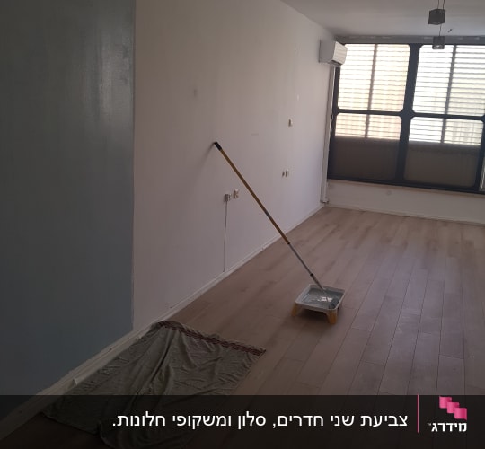 קיר צבוע חלקית, מגש צבע ומברשת על הרצפה